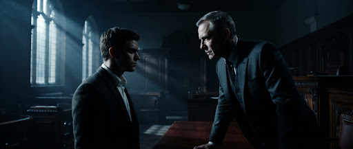 Two actors facing each other in a shadowy wood-panelled courtroom